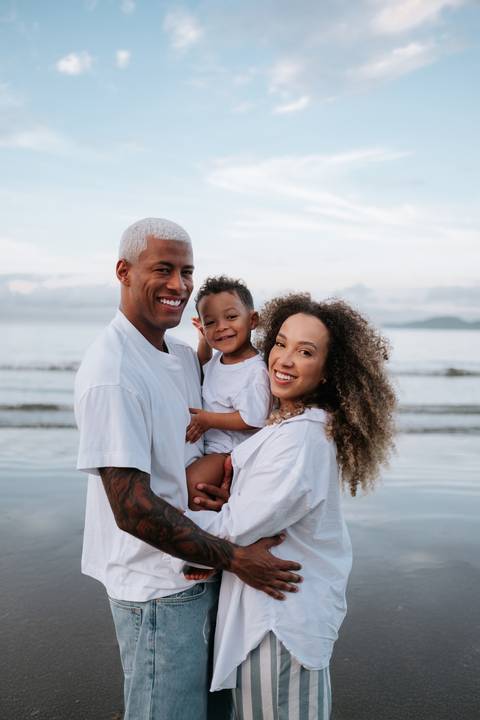 Foto da família unida sorridente à beira-mar.'