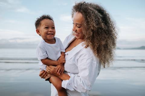 Foto da mãe e filho em um momento de risada espontânea na areia.'