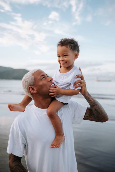 Foto do pai olhando para cima e sorrindo para o filho nos ombros.'