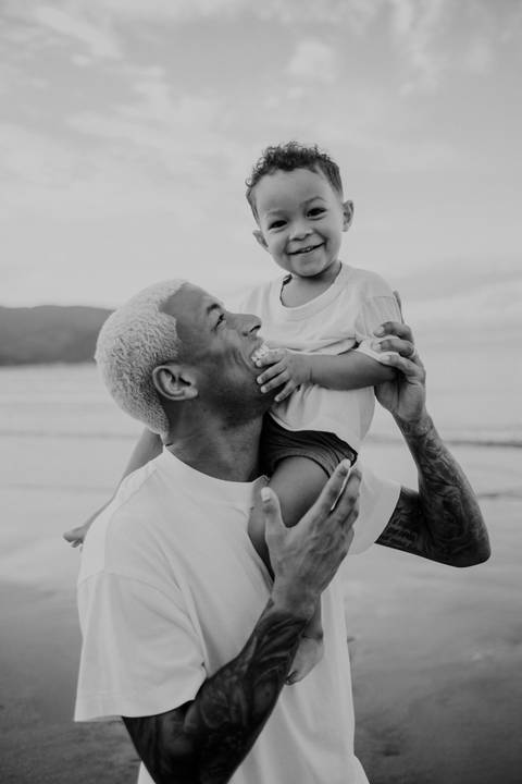 Foto em preto e branco do pai brincando com o filho nos ombros.'
