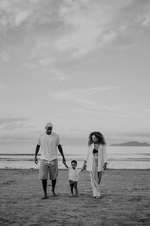 Foto em preto e branco da família caminhando unida pela areia molhada.'
