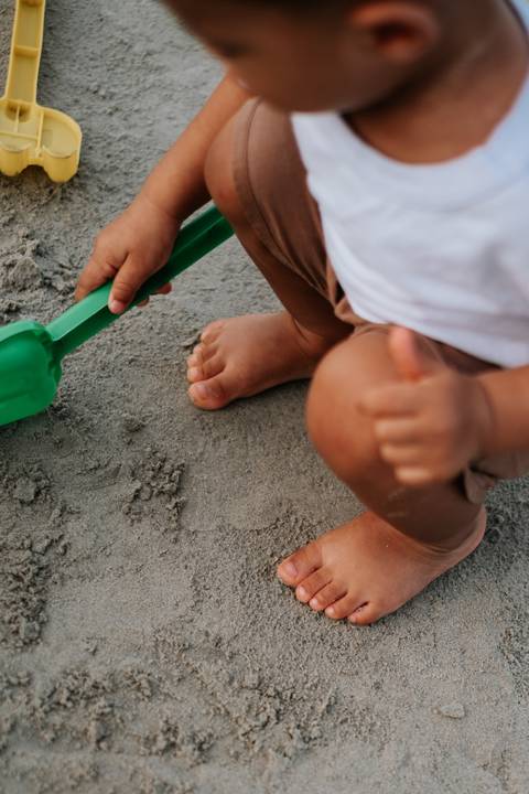 Foto em macro das mãos e pés do bebê brincando na areia molhada.'