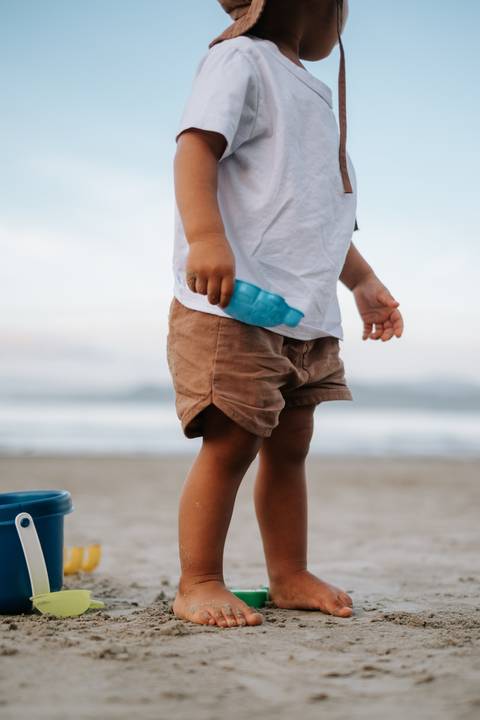 Foto em detalhe do bebê segurando brinquedos de praia coloridos.'