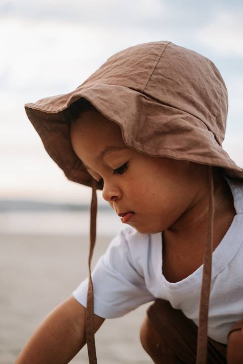 Foto em close do perfil do bebê com o chapéu de praia.'