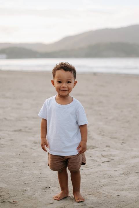 Foto de close do bebê em pé na areia sem auxílio, olhando para a câmera.'