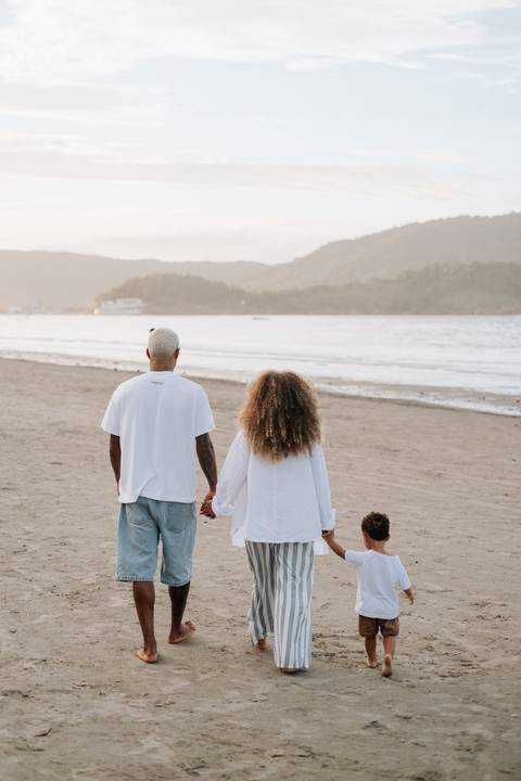Foto da família de costas caminhando em direção ao mar no fim de tarde.'