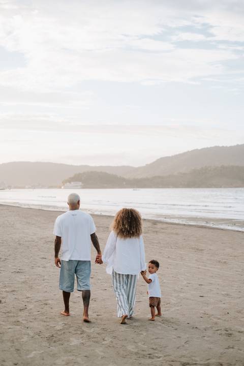 Foto panorâmica da família caminhando unida pela orla da praia.'