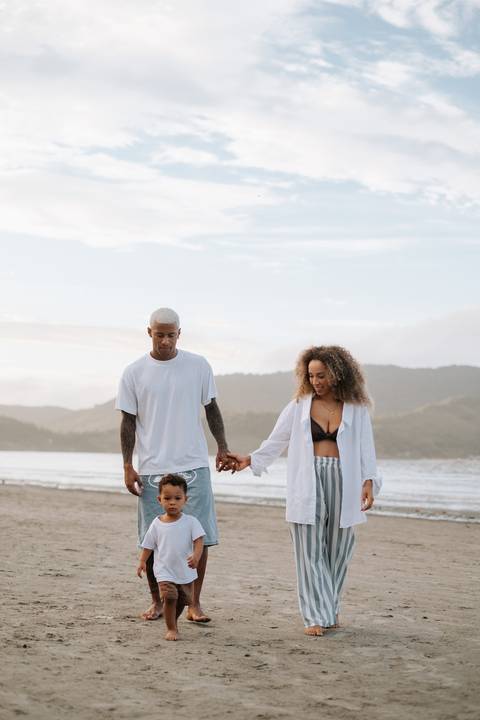 Foto do casal de mãos dadas com o filho pequeno entre eles.'