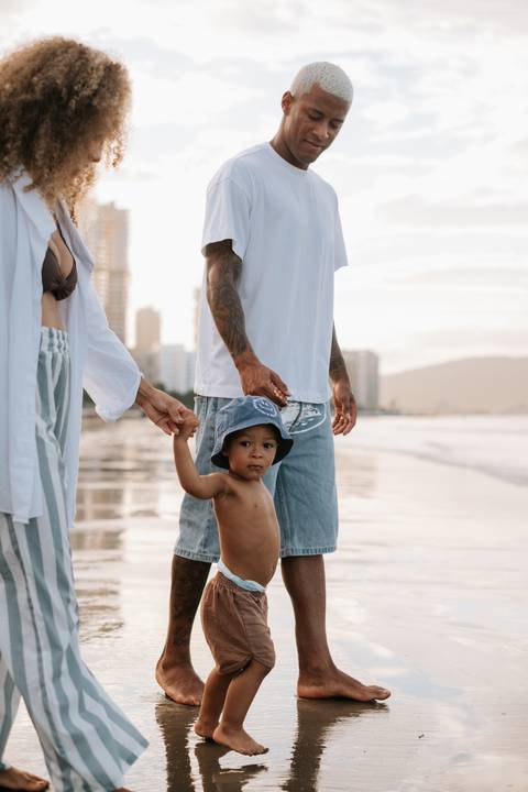 Foto aproximada do bebê de chapéu azul segurando a mão do pai.'