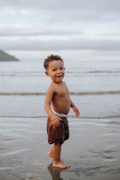 Foto do bebê em pé na areia olhando para o horizonte.'