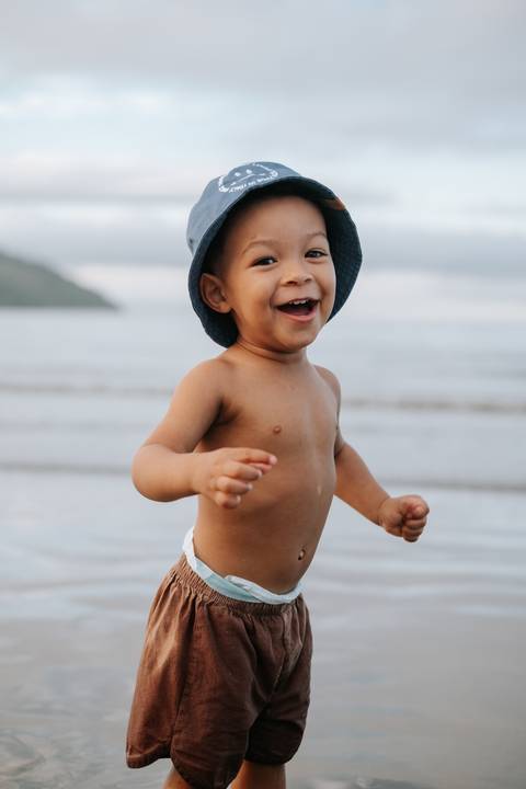 Foto do bebê rindo e caminhando livremente pela praia.'