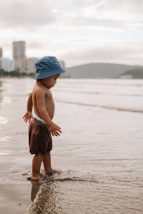 Foto de perfil do bebê observando as ondas na praia.'