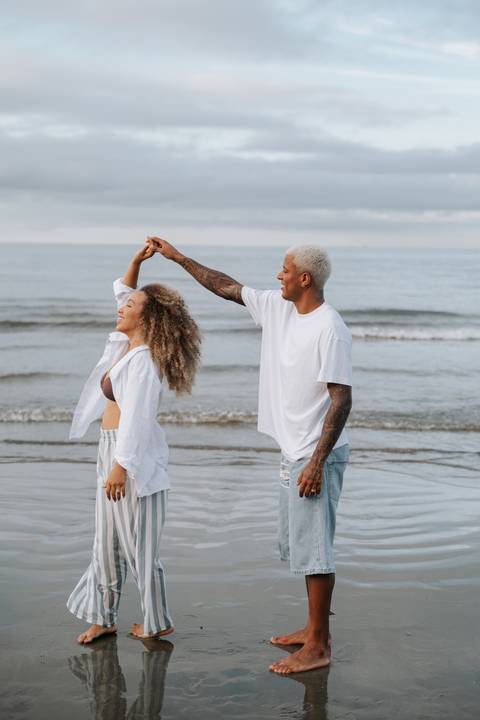 Foto do casal dançando e sorrindo na areia.'