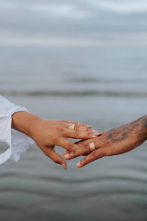 Foto em detalhe das mãos do casal entrelaçadas mostrando as alianças.'