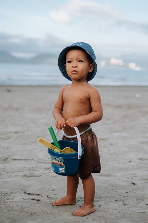 Foto do bebê segurando um balde azul com pazinhas de brinquedo.'