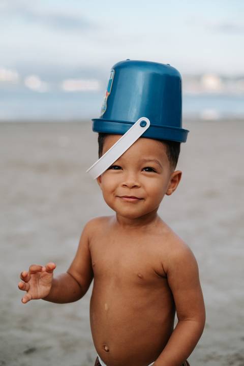 Foto divertida do bebê com o balde azul na cabeça sorrindo.'
