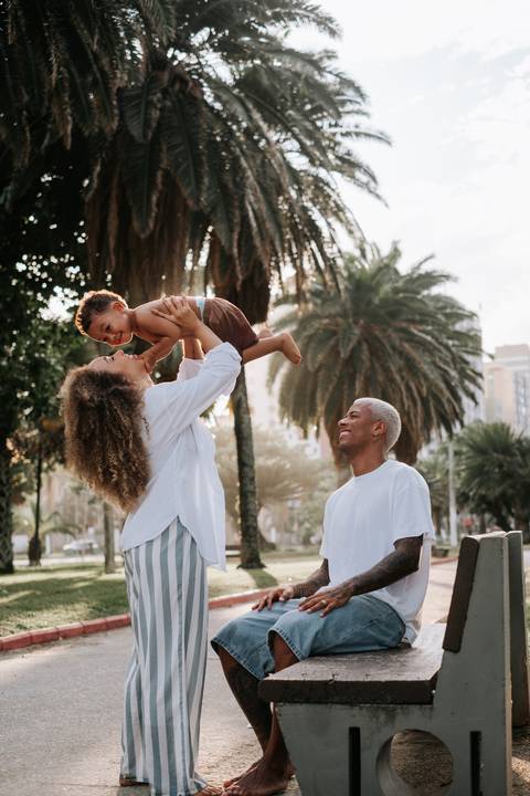 Foto do casal de costas em pose descontraída erguendo o filho no alto.'