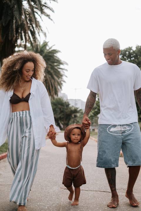 Foto do casal de mãos dadas com o filho pequeno caminhando por calçadão no parque.'