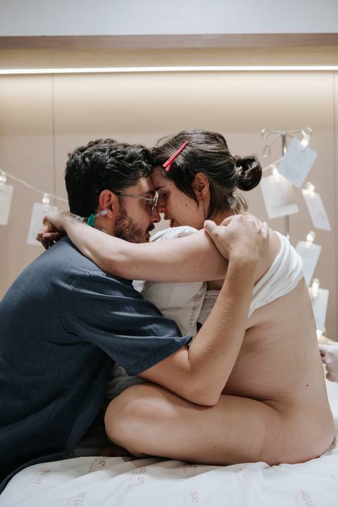 Foto de abraço acolhedor entre o casal em meio ao cenário preparado para o parto.'
