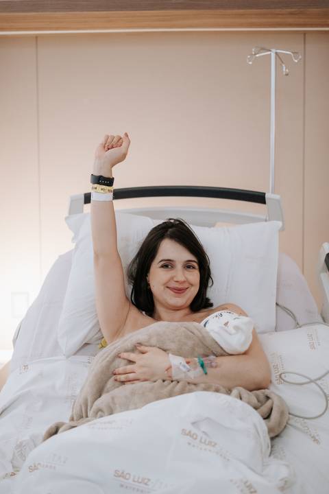Foto da mãe com o braço erguido celebrando a força e a vitória do nascimento.'