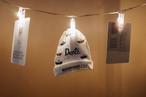 Foto de detalhe de um varal de luzes com fotos e a touquinha do bebê com o nome 