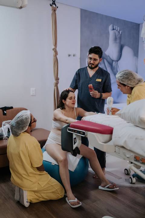 Foto panorâmica da sala de parto com a gestante sendo amparada pela equipe e acompanhante.'