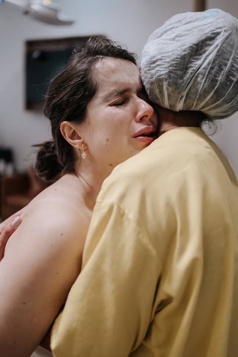 Foto da parturiente chorando e sendo abraçada por uma profissional da saúde.'