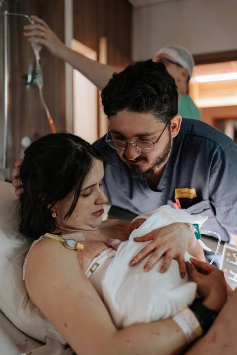 Foto do casal maravilhado observando o recém-nascido Davi no colo materno.'