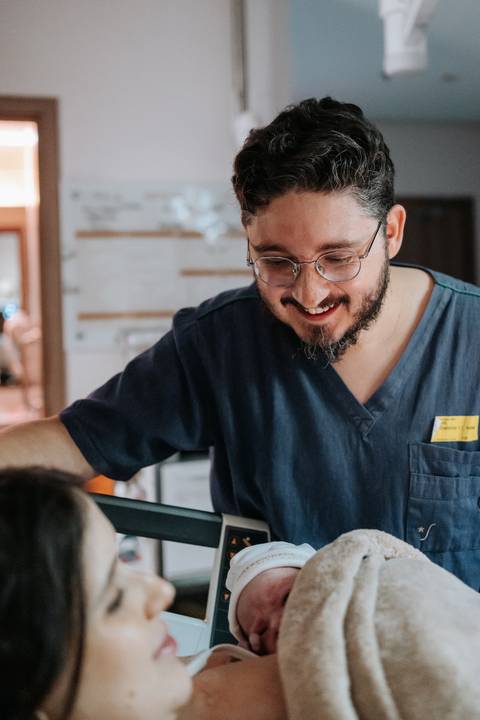 Foto do pai sorridente e emocionado observando o filho recém-nascido.'