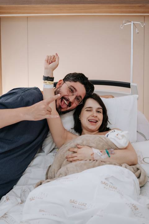 Retrato do casal sorridente com o bebê protegido em uma manta.'