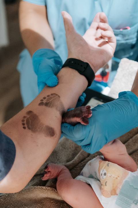 Foto em detalhe do carimbo dos pezinhos do bebê no braço de um familiar.'