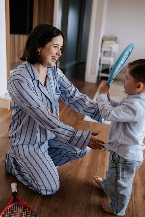 Foto da mãe agachada interagindo e dando atenção ao filho mais velho.'