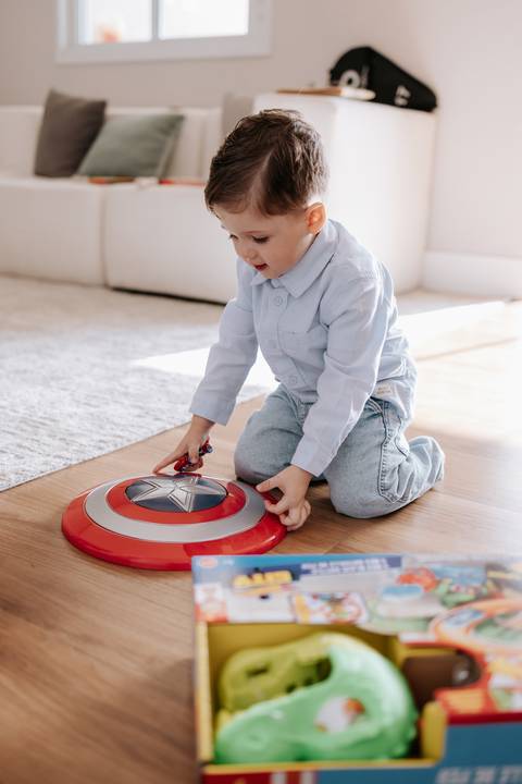 Foto do irmão mais velho brincando com um escudo do Capitão América no tapete.'