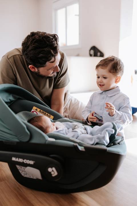 Foto do pai e do filho mais velho observando o bebê dormir com curiosidade.'