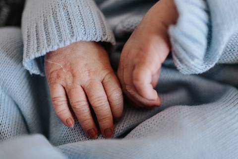 Foto em detalhe das mãos pequenas e delicadas do recém-nascido.'
