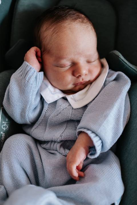 Foto aproximada do bebê dormindo usando uma roupinha de tricô azul claro.'
