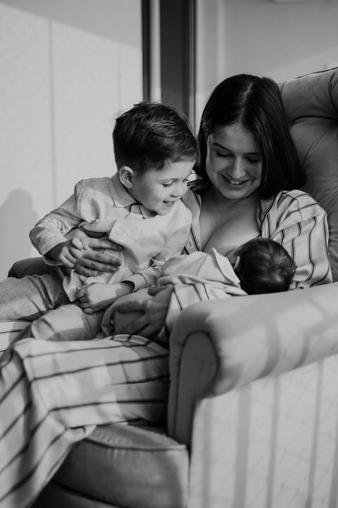 Foto em preto e branco da mãe em momento de carinho com os dois filhos.'