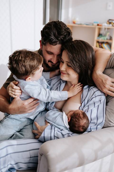 Retrato afetivo da família completa abraçada durante o momento da amamentação.'