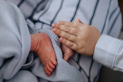 Foto em detalhe da mão do irmão mais velho tocando o pé do bebê.'