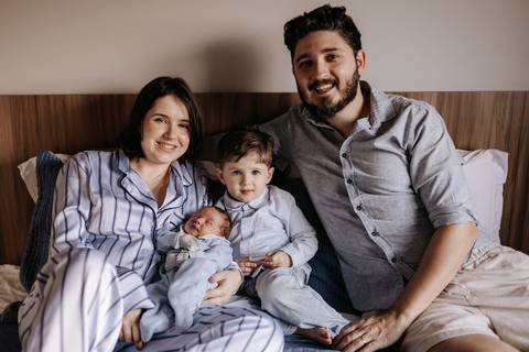 Retrato oficial da família (pai, mãe e dois filhos) sorrindo na cama.'