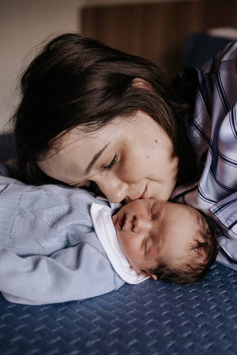 Foto aproximada da mãe beijando a bochecha do recém-nascido.'