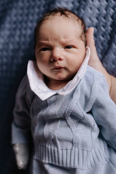 Foto em detalhe do bebê usando roupinha de tricô com gola bordada.'