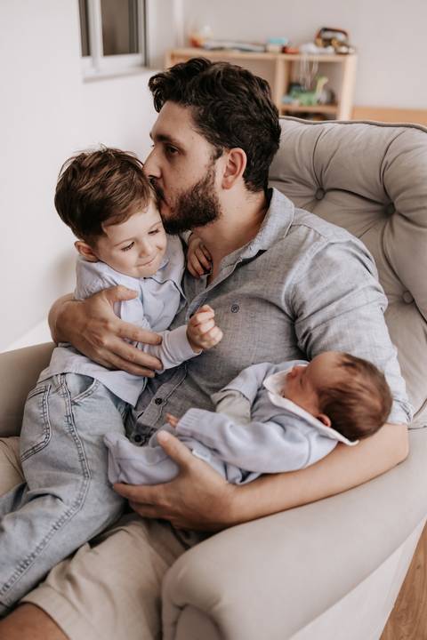 Foto do pai abraçando o filho mais velho enquanto segura o bebê.'