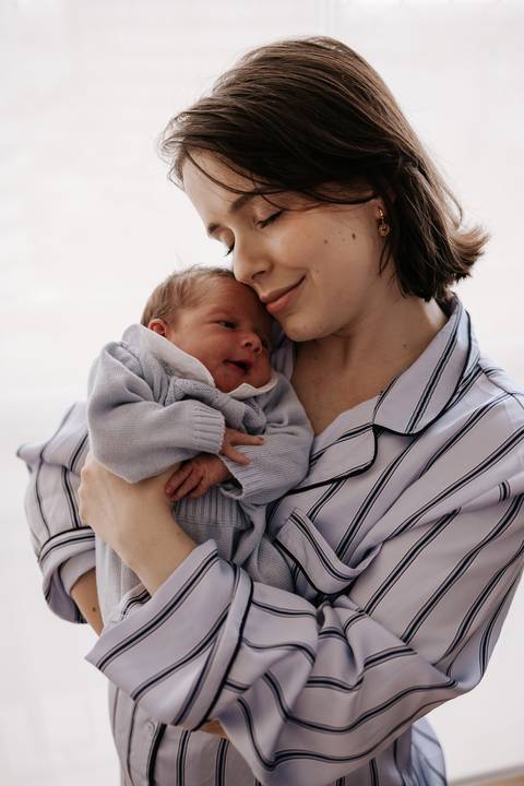 Foto da mãe segurando o bebê no colo e sorrindo serenamente.'
