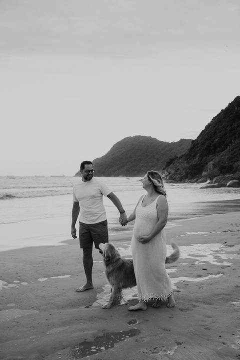 Foto em preto e branco do casal caminhando sorrindo na praia.'