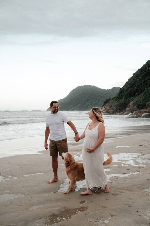 Foto do casal de mãos dadas caminhando na areia com as montanhas ao fundo.'