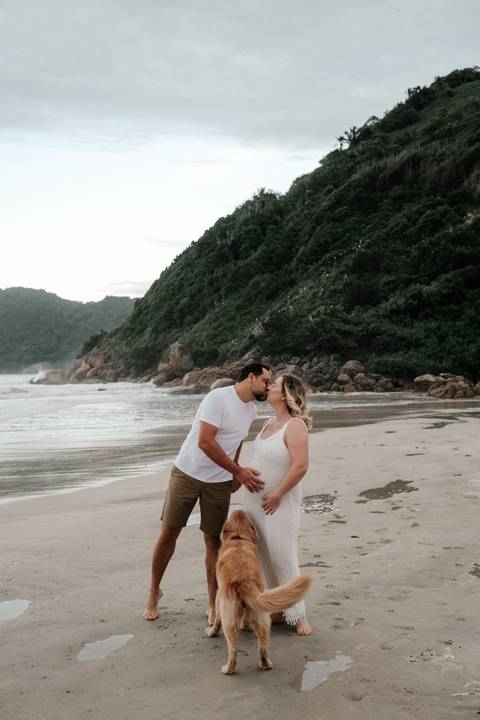 Foto aproximada do casal trocando um beijo carinhoso na beira da água.'