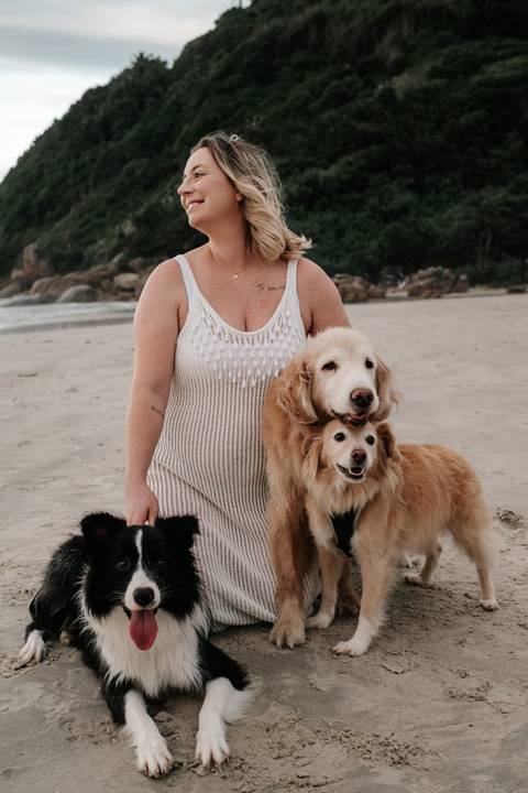 Close da gestante abraçando carinhosamente seus cães na praia.'
