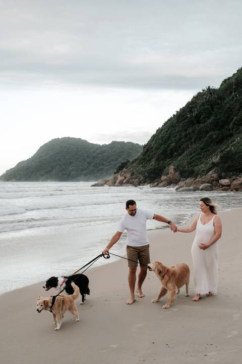 Foto panorâmica do casal de mãos dadas na areia, capturando a imensidão do cenário.'