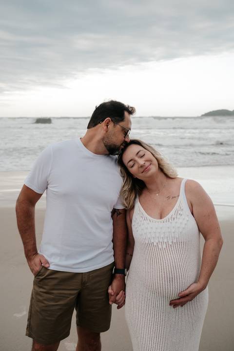 Retrato aproximado do pai beijando a testa da gestante com os olhos fechados.'